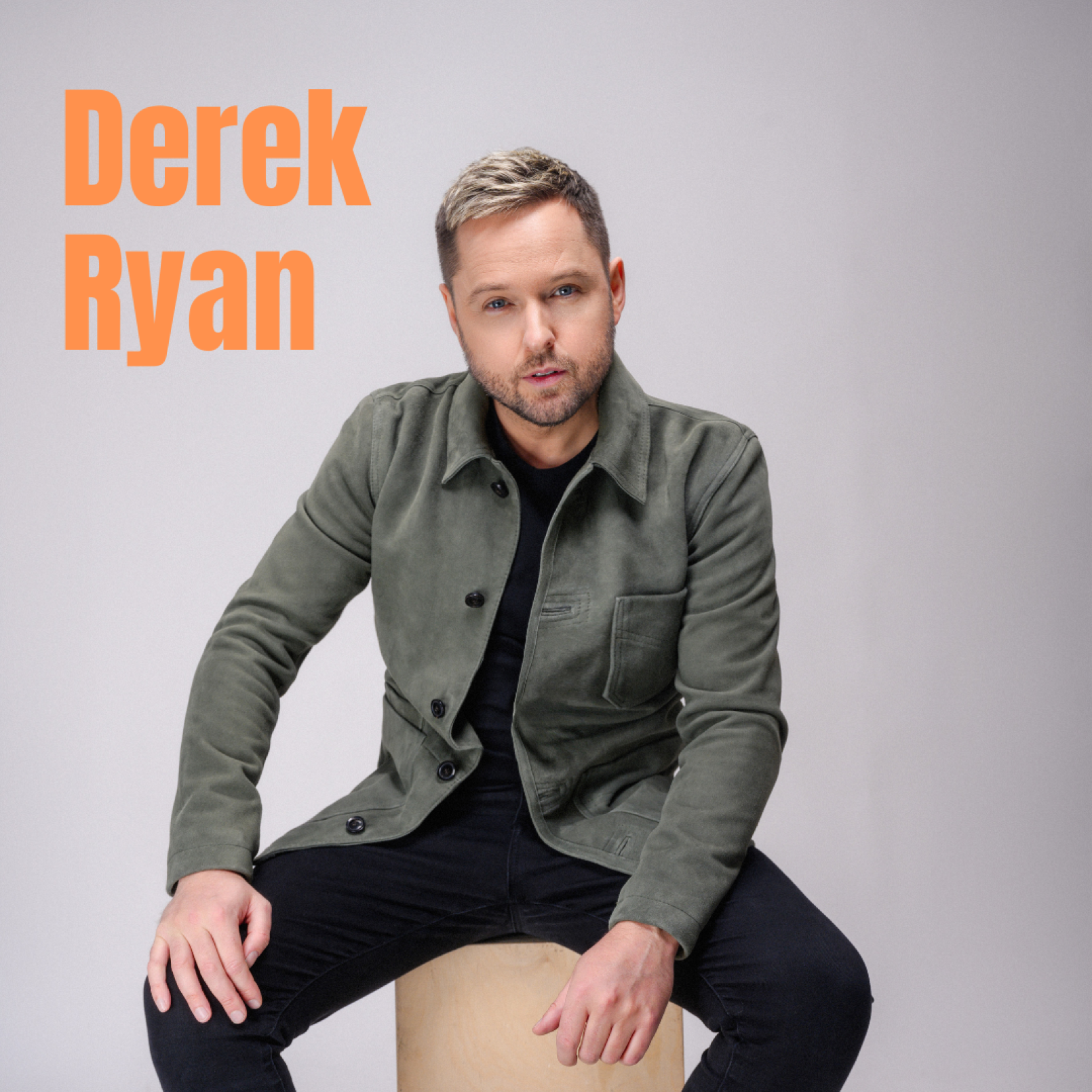 A man with short hair and a beard sits on a stool wearing a green jacket and black pants. The background is grey. "Derek Ryan" is written in orange text.