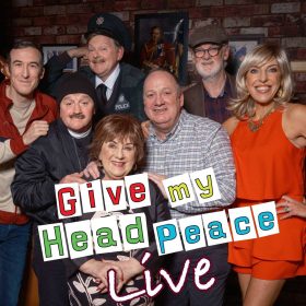 The image features a group of seven people smiling in front of a brick wall decorated with framed pictures. Text overlay reads "Give my Head Peace Live." The mood is playful and upbeat.