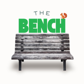 Weathered wooden bench with metal legs. Above it, "The Bench" is written in bold green letters with a small squirrel sitting on the "N." Simple and inviting.
