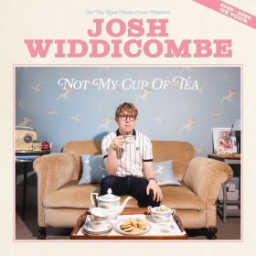 Josh Widdicombe sitting on a beige sofa drinking tea, surrounded by a vintage tea set. Blue bird-patterned wallpaper. Text: “Josh Widdicombe: Not My Cup of Tea”. Lighthearted tone.